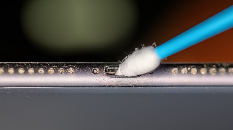 A cotton swab cleaning an iPhone's charging port