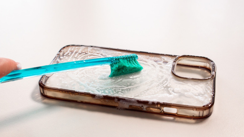 Transparent phone case being cleaned with warm water and soap and soft brush.