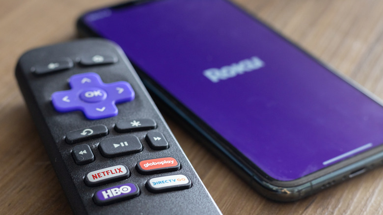 A Roku remote next to a smartphone loading the Roku app on a table