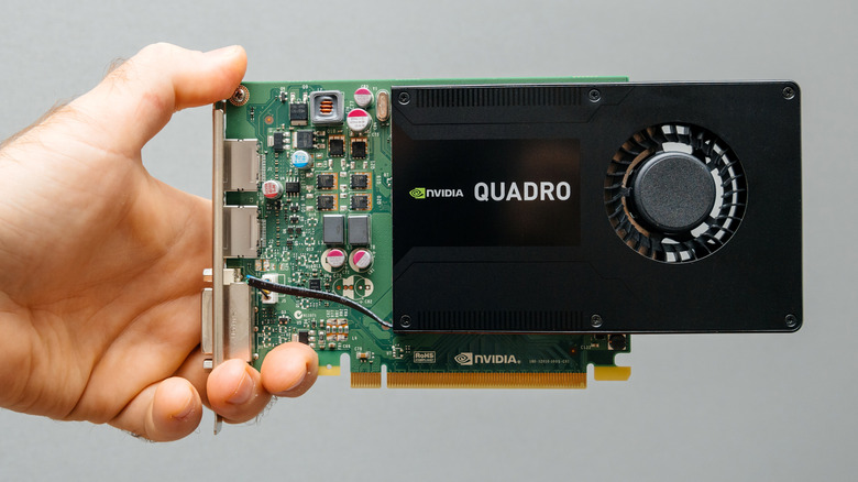 A NVIDIA Quadro graphics card is held in an individual's left hand against a gray backdrop