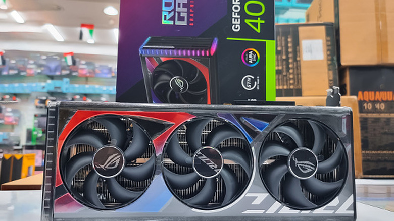 A GeForce RTX 4090 GPU sits in front of its packaging in what appears to be an electronics store, there are several boxes behind the surface holding the card and its box