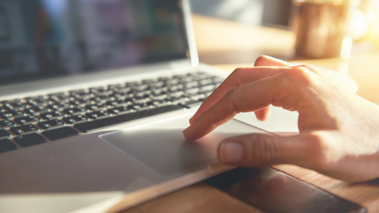 A hand touching a laptop trackpad.