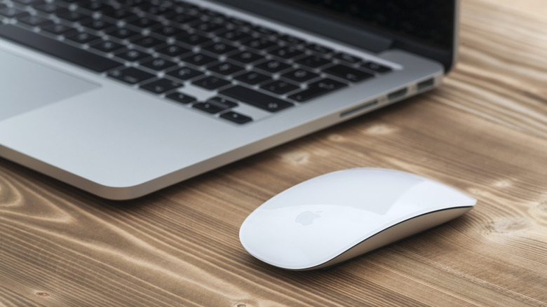 An Apple MacBook on a wood table with a Magic Mouse beside it.