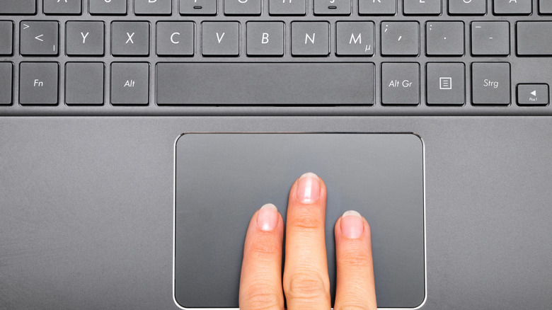 Three fingers on a laptop keyboard's trackpack.
