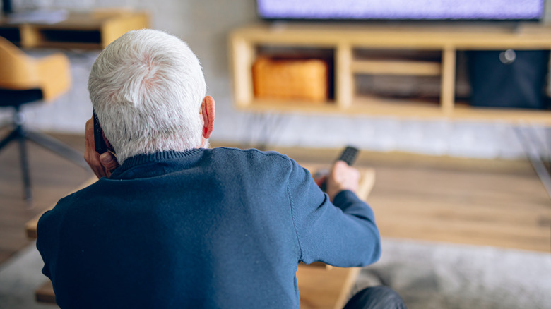 Old man on the phone trying to fix TV settings