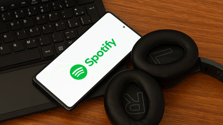 Spotify logo on a mobile device next to a laptop and headset on a wooden table