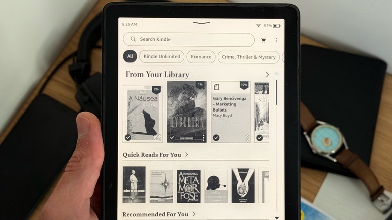 A hand holding an Amazon Kindle with its display showing the device's Home Screen
