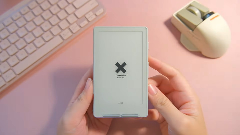 Hand holding Xteink e-reader showing Crosspoint booting