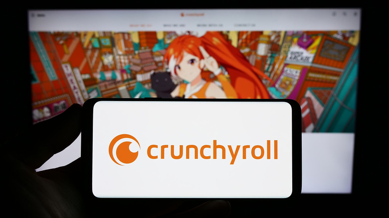 Crunchyroll logo on mobile device with a blurred backdrop of titles anime shows on tv