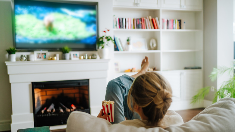A lady sitting on sofa watching content on her smart TV while holding a pop-corn box