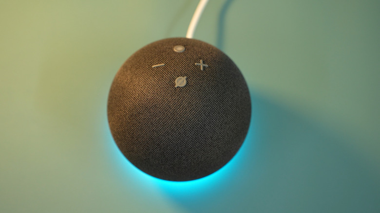 A black Amazon Echo Dot sits against a blue-green backdrop, the device's status bar is casting a blue light