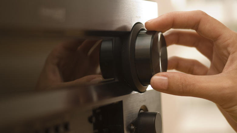 A person adjusting a control knob on an AV receiver.