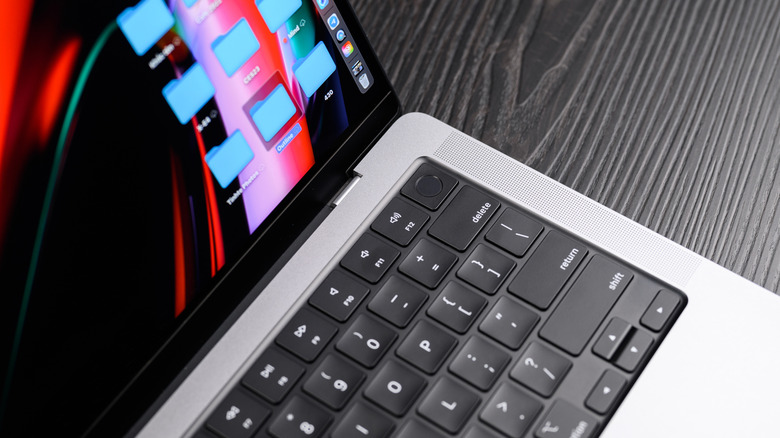 A silver MacBook Pro displaying its desktop sits on a black wooden material, the photo is stylized to only show a portion of the MacBook