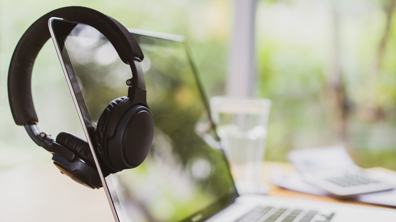 A pair of black headphones hang off the screen of silber MacBook laptop