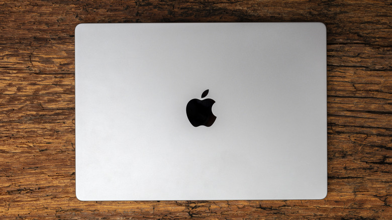 A silver MacBook Pro with its lid closed sits on a wooden backdrop, the device's Apple logo is prominent in the photo