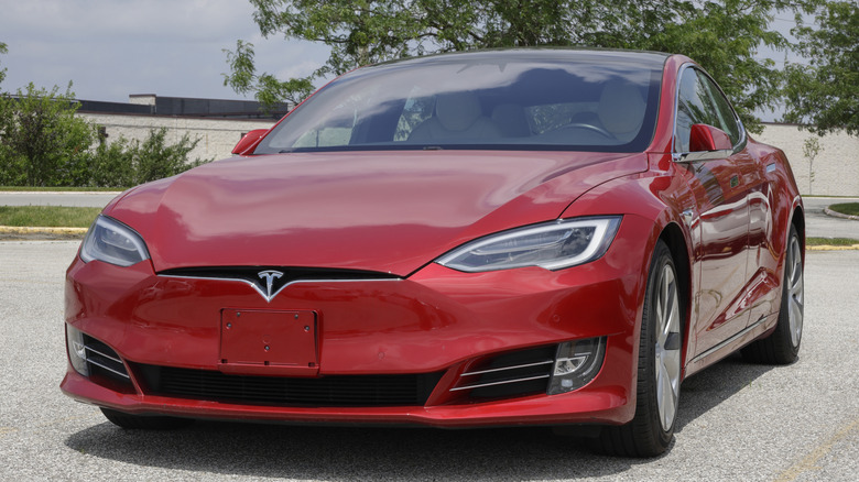 A red Tesla sitting outside, several trees are behind the vehicle