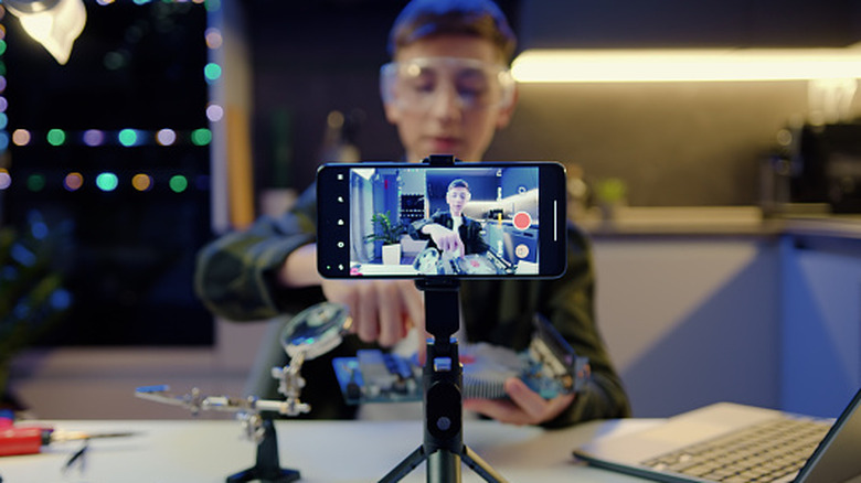 Focus on screen of smartphone. Young man is live streaming from his iPhone.