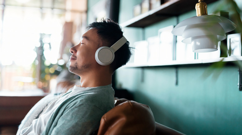 A person leaning back, listening to headphones on a couch
