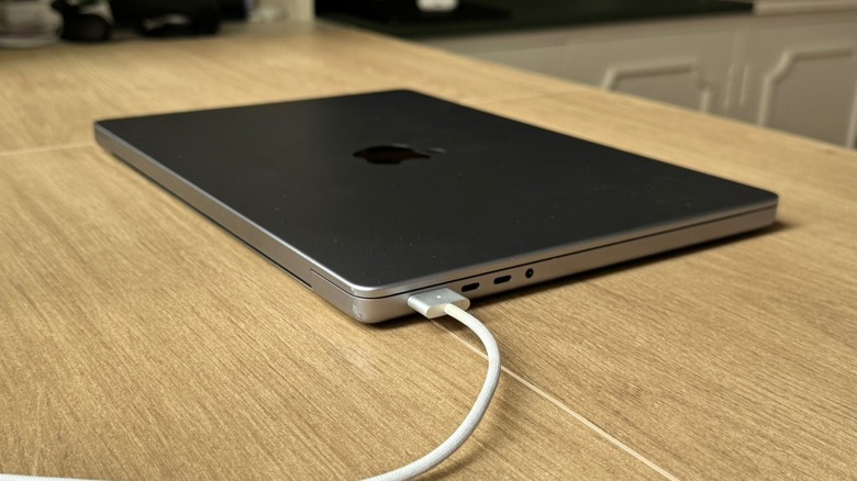 A MacBook Pro on a wooden table being charged with a MagSafe cable