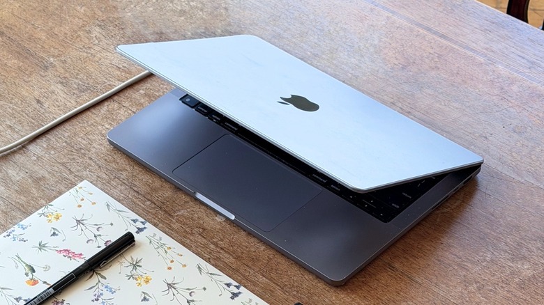 A half-closed MacBook Pro on a wooden table being charged via USB-C cable
