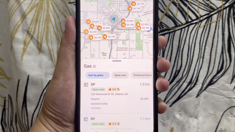 A hand holding a phone showing Waze with gas stations and their gas prices