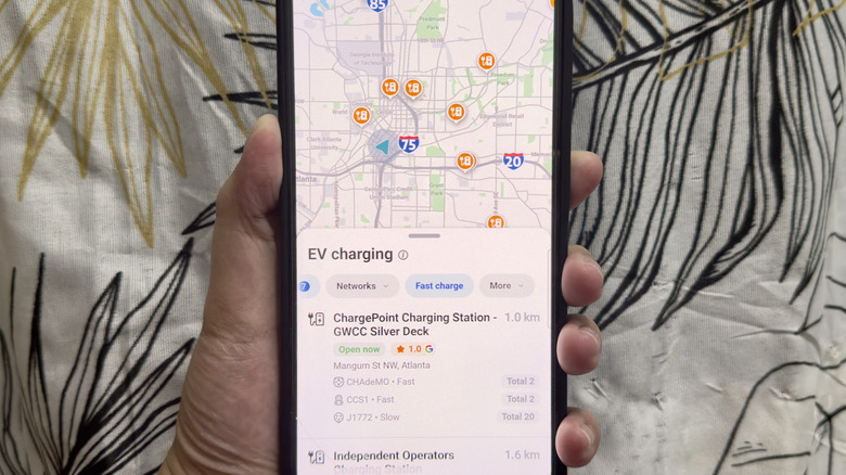A hand holding a phone showing EV charging stations with charger details