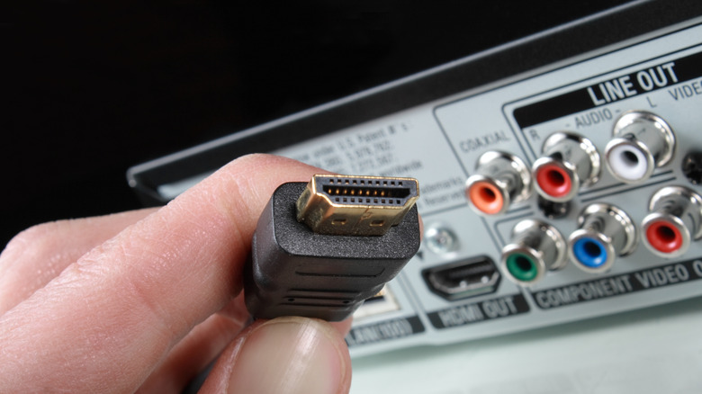A person holding up an HDMI cable near a Blu-ray player.