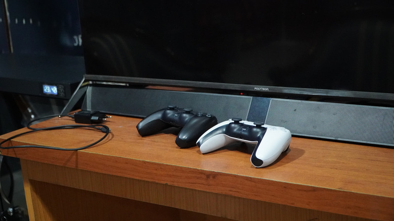 A soundbar placed below a TV on a TV stand. Two game controllers are placed in front of it.