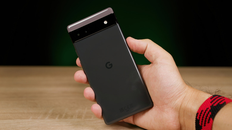 A man's hand holding a Google Pixel 6a on a wood table
