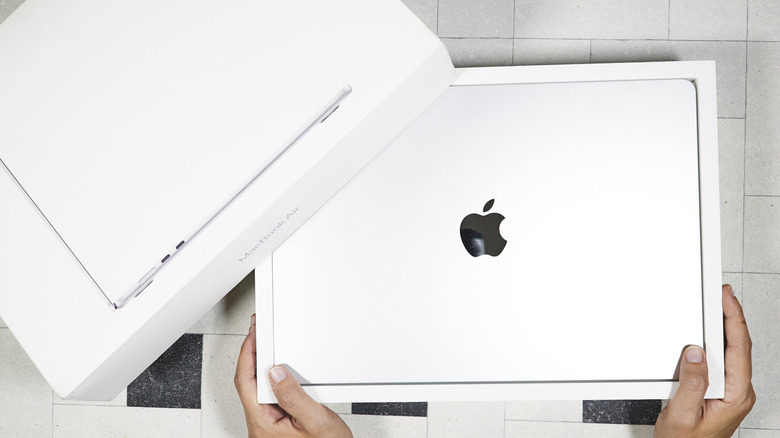 Two hands on a white box with the Apple logo and an Apple MacBook inside.