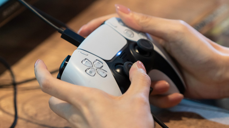 a person holding a PlayStation 5 DualSense controller while the USB-C cable is plugged in