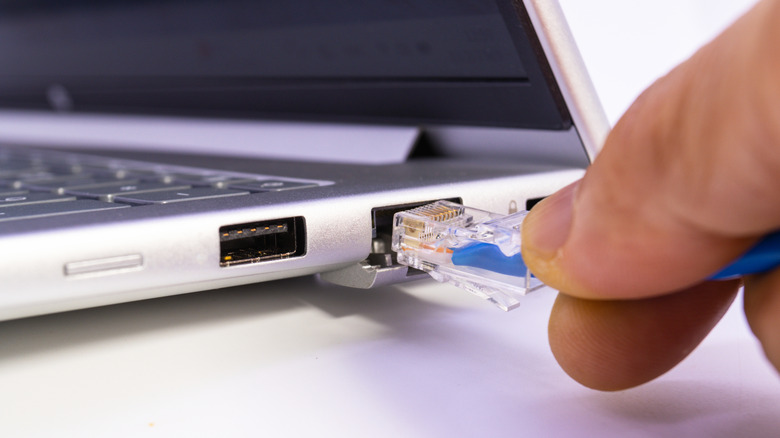 A hand plugging an ethernet cable into a laptop