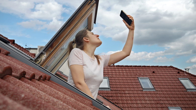 A woman trying to improve her phone signal by holding her phone high up on the roof