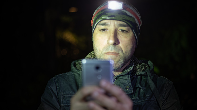Man in survival gear checking phone at night