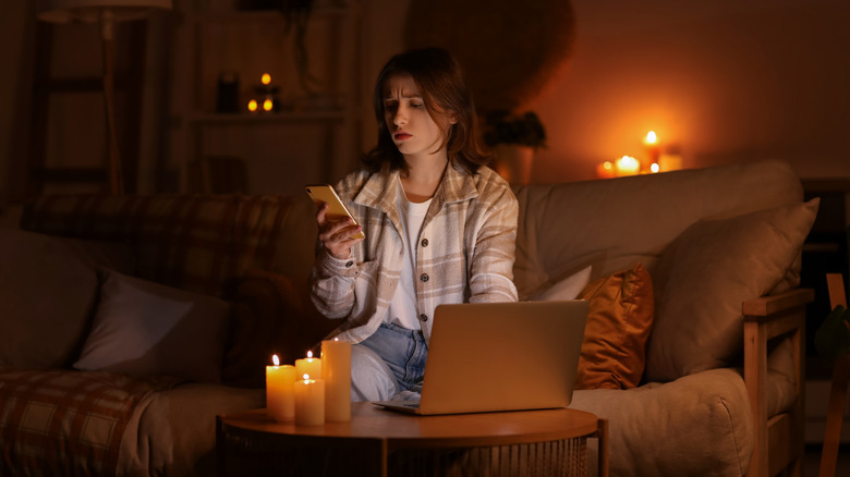 Young woman using phone and computer during blackout