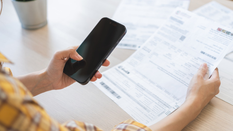 Person looking at a bill while holding a cell phone