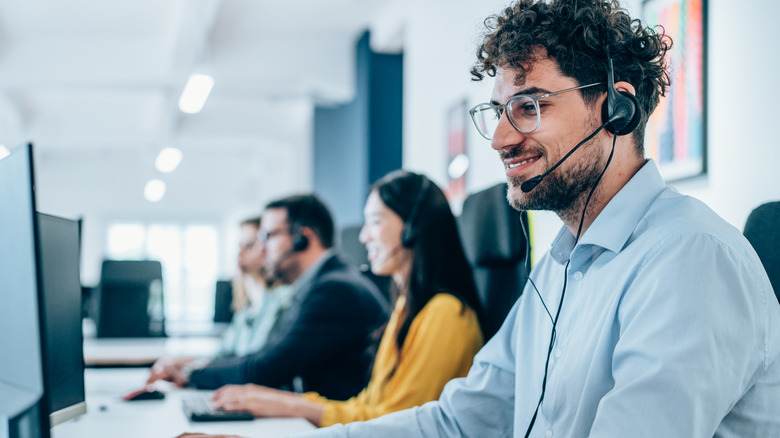 Several call center workers sitting side by side at a long shared desk