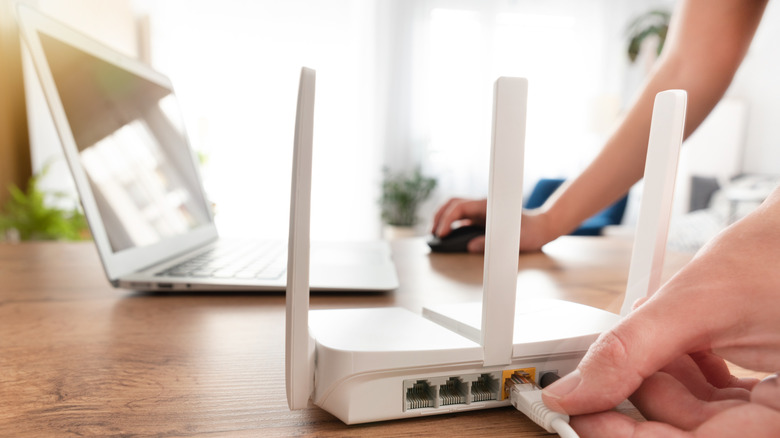 A picture of someone connecting an Ethernet cable to router while using a laptop.