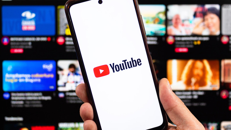 A person holding a smartphone showing the YouTube logo.