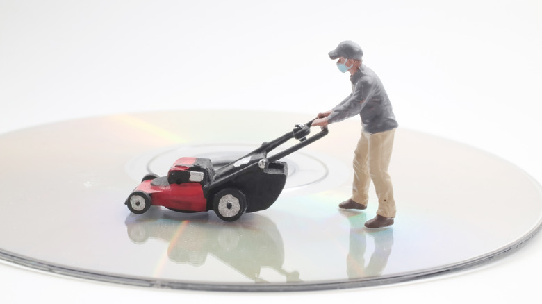 Miniature person mowing the surface of a compact disc.