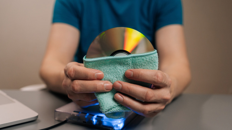 Hands cleaning an optical disc with a soft cloth.