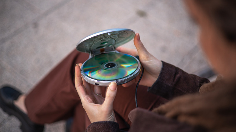 Person holding a portable CD player with a writable disc visible inside.