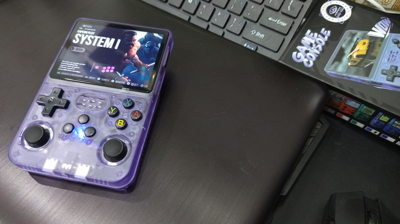 Retro handheld with transparent purple shell resting on a desk with screen on.