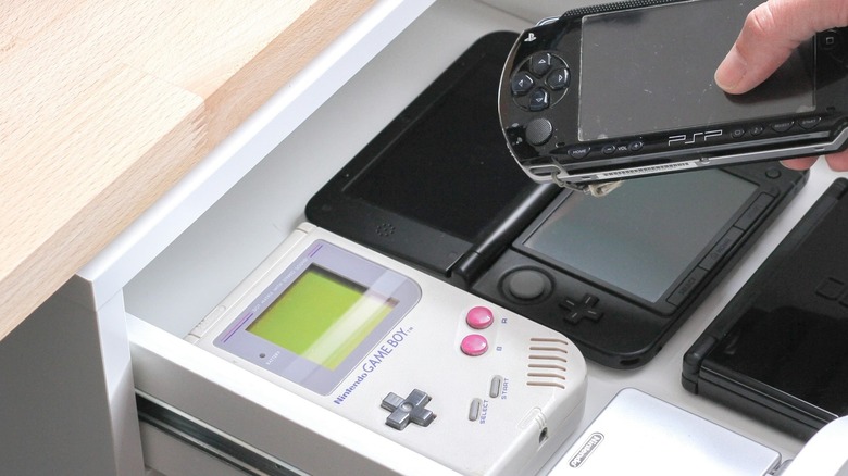 Desk drawer open with retro handhelds visible and hand removing a PSP.