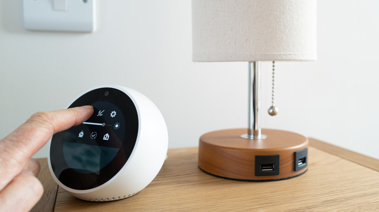 A person's hand reaching out to interact with an Echo Spot Alexa speaker from Amazon.