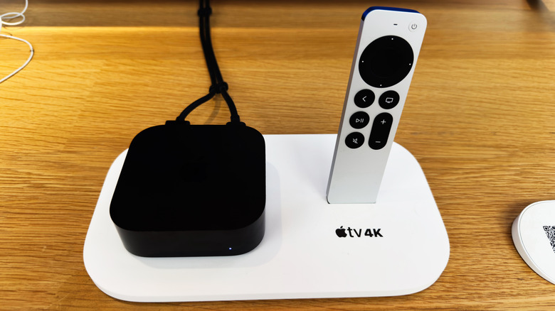 Apple TV 4K device and its remote on a white dock beside a TV