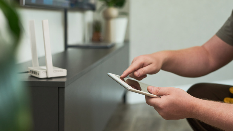 A person holding a tablet configuring a router placed on a wooden cabinet