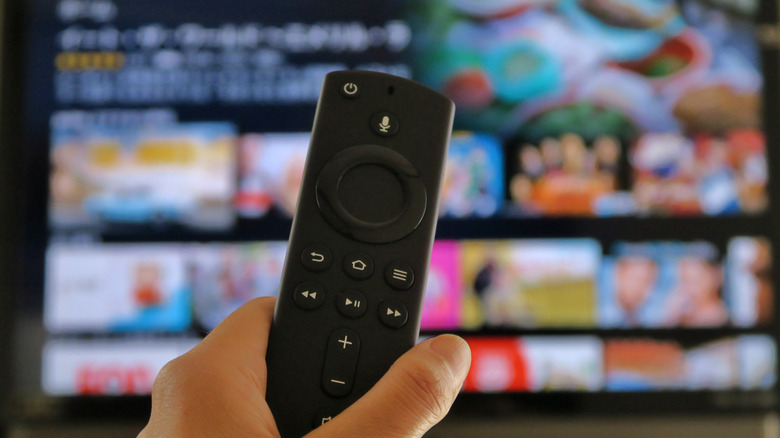 A person holding a Fire TV remote with an out of focus TV in the background