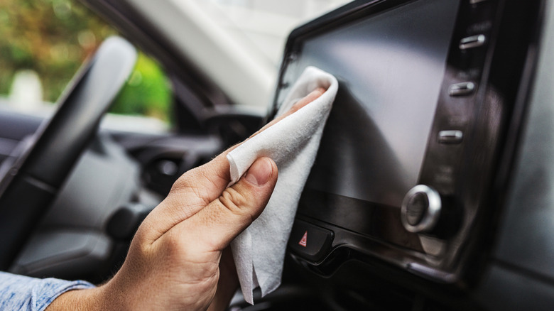 A person using a microfiber cloth to wipe a vehicle infotainment screen.