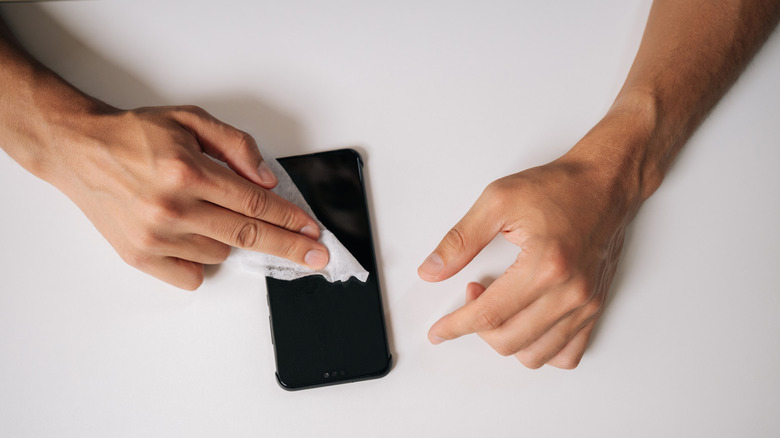 A person wiping the screen of a phone with a paper cloth